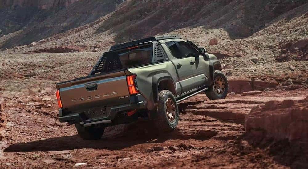 A green 2024 Toyota Tacoma Trailhunter is shown driving on rocks.