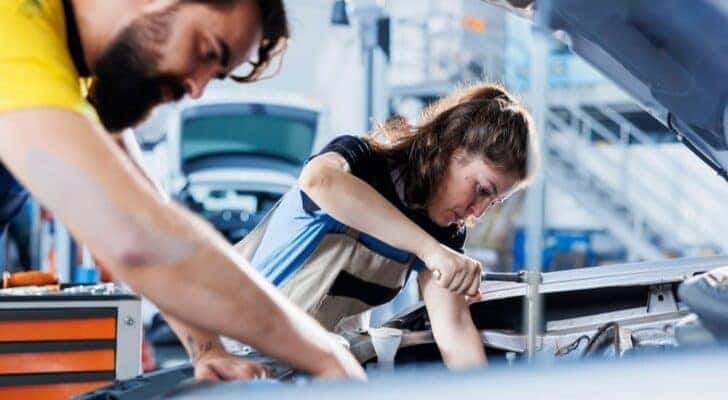 Two mechanics are shown working on an alternator replacement.