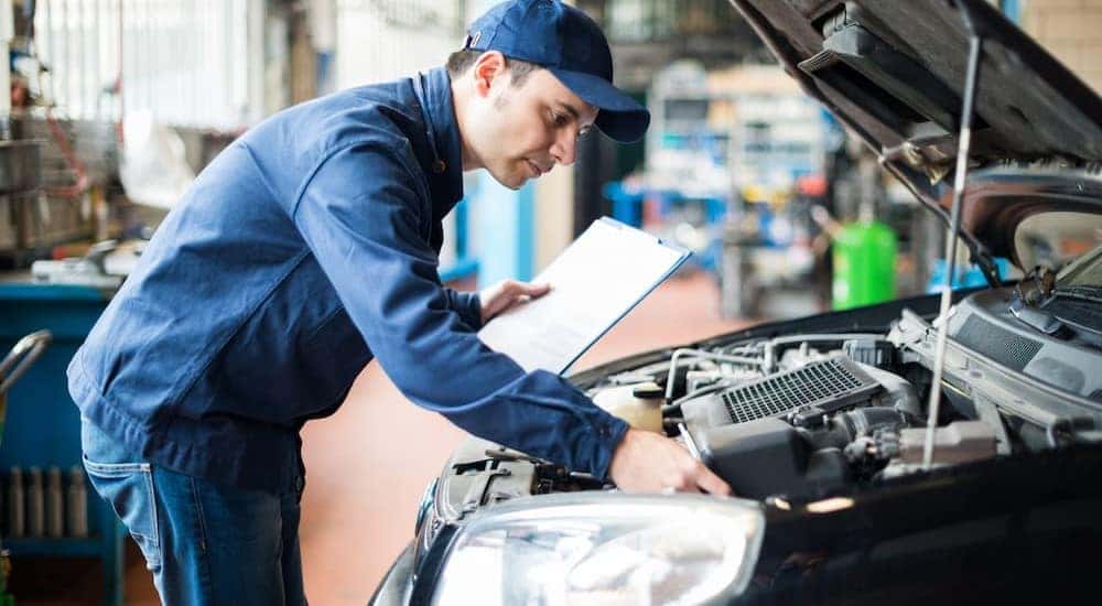 A mechanic is shown holding a clipboard and looking at an engine.
