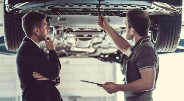 A mechanic and customer are shown looking at the undercarriage of a vehicle.