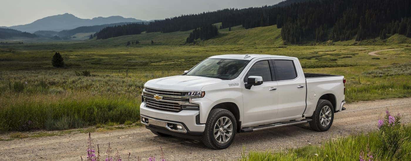 A white 2021 Chevy Silverado 1500 High Country is shown driving on a dirt road.