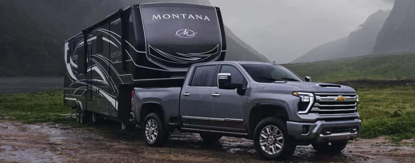 A gray 2024 Chevy Silverado 2500 HD High Country is shown towing a trailer on mud.