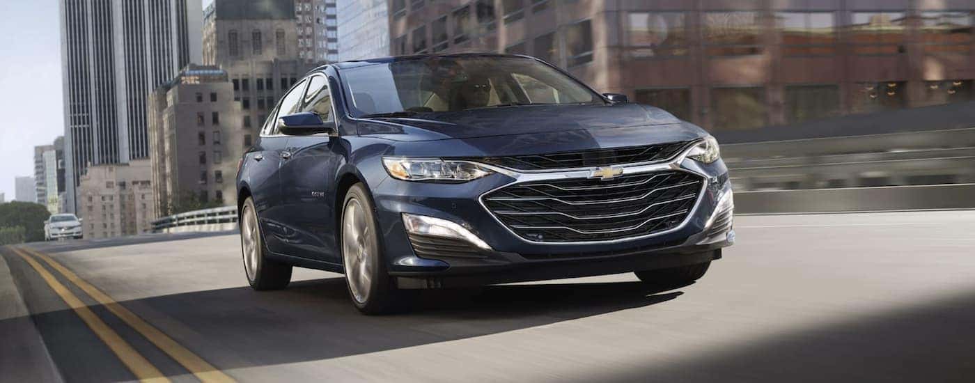 A blue used 2022 Chevy Malibu driving in a city