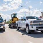 Two 2018 Chevy Silverado 2500 HD towing heavy machinery down the road.