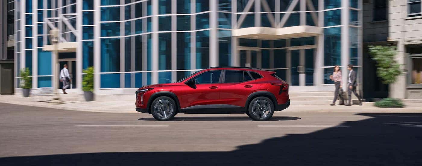 Side of a red 2026 Chevy Trax RS driving down a road.