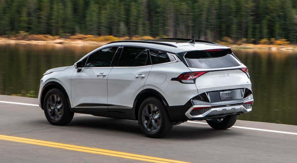 A white 2024 Kia Sportage Hybrid driving by a lake.