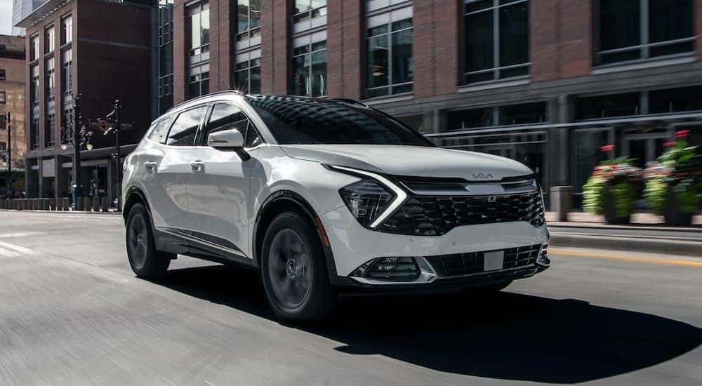 A white 2024 Kia Sportage Hybrid driving in a city.