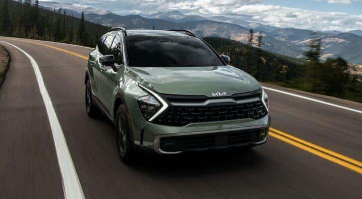 A green 2023 Kia Sportage is driving on a mountain road.