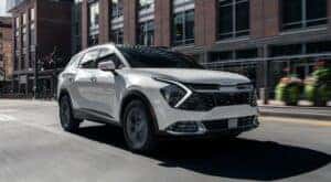 A white 2024 Kia Sportage Hybrid driving in a city.