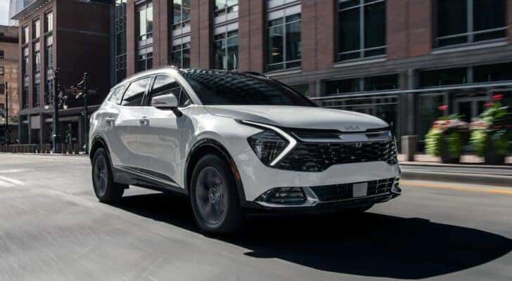 A white 2024 Kia Sportage Hybrid driving in a city.
