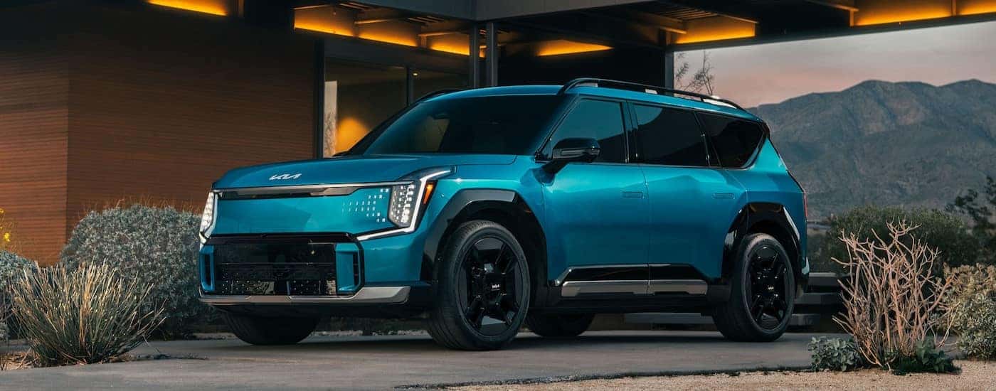 A blue 2024 Kia EV9 is shown parked on a driveway.