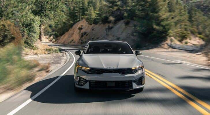 A gray 2024 Kia K5 is shown driving to a Kia dealer near Alcoa.