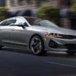 A grey 2024 Kia K5 driving from a Kia dealer in Knoxville.