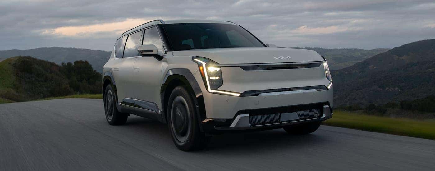 A white 2024 Kia EV9 is driving on a winding road.