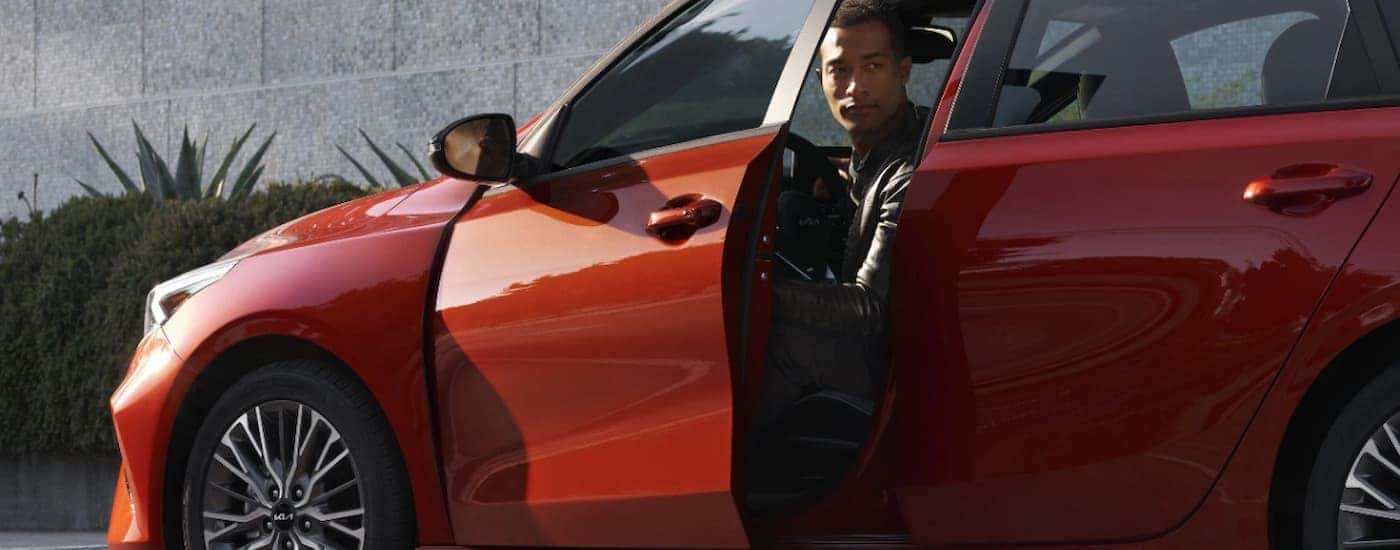 A man is getting out of an orange 2024 Kia Forte.