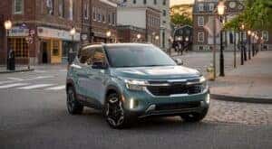 A blue 2025 Kia Seltos for sale is shown driving in a city.