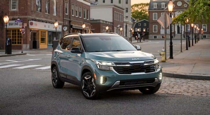 A blue 2025 Kia Seltos for sale is shown driving in a city.