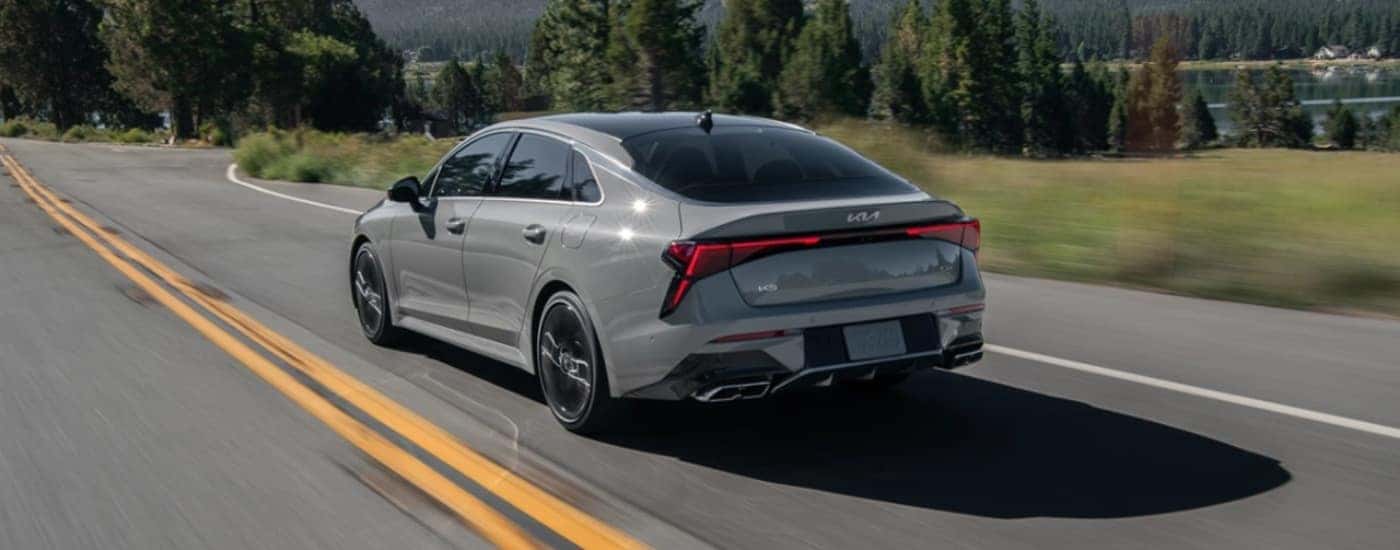 A grey 2025 Kia K5 GT driving past a lake.