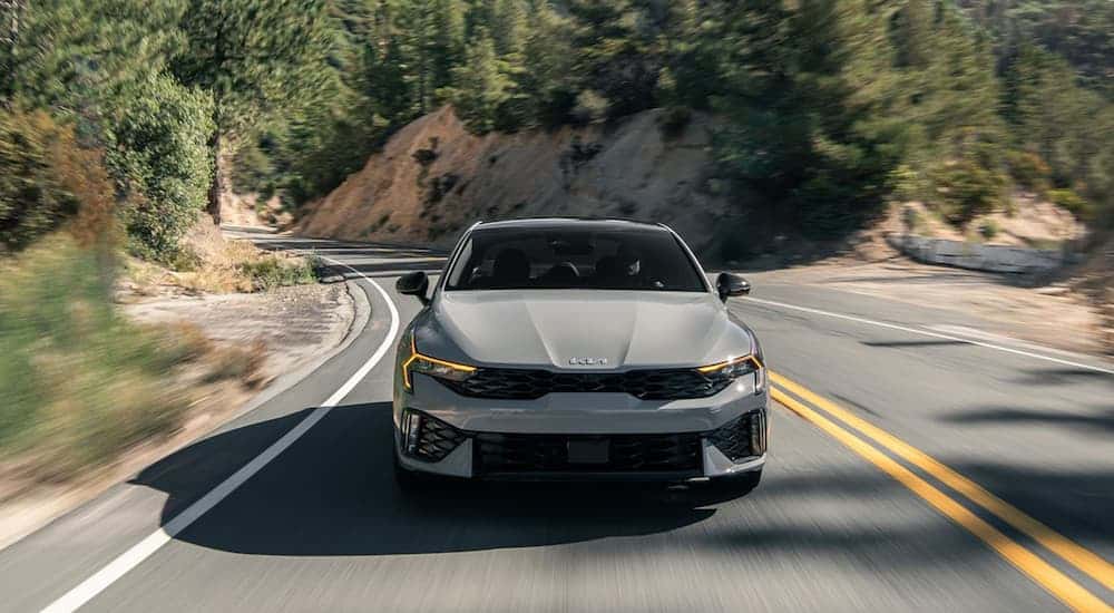 Front of a grey 2025 Kia K5 driving down an open road.