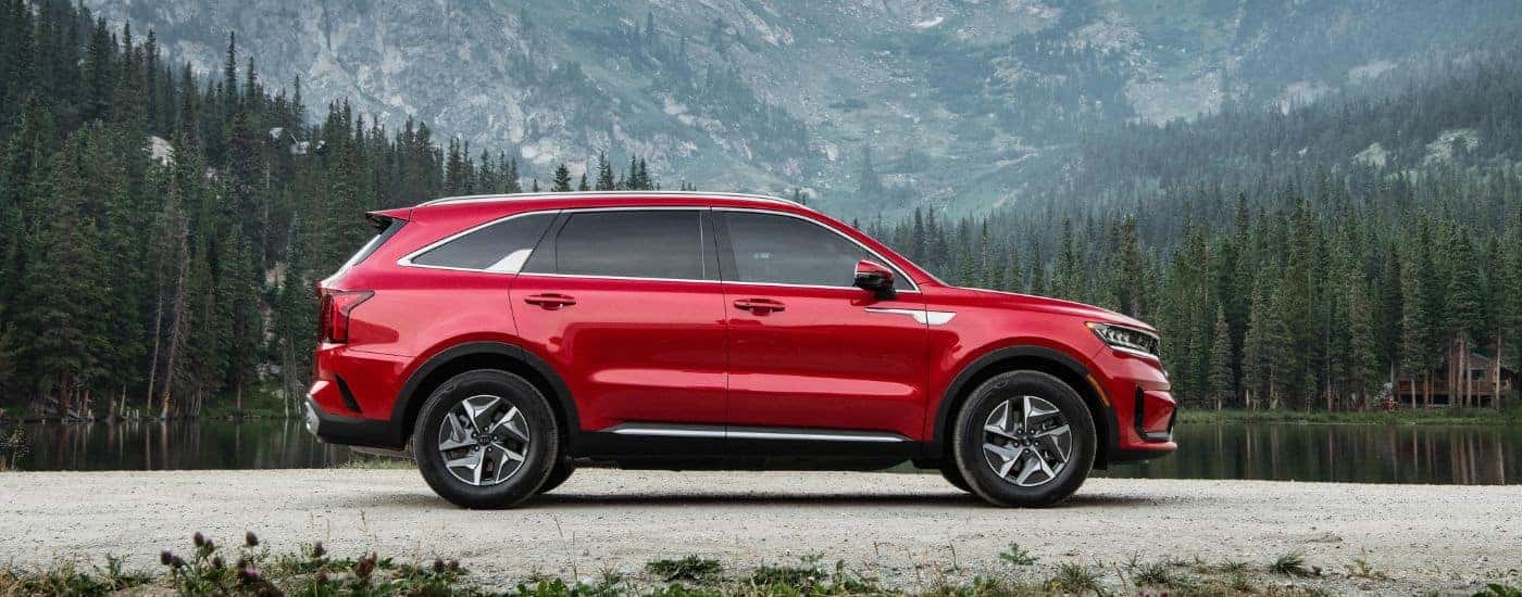Side view of a red 2023 Kia Sorento Hybrid parked by a lake.