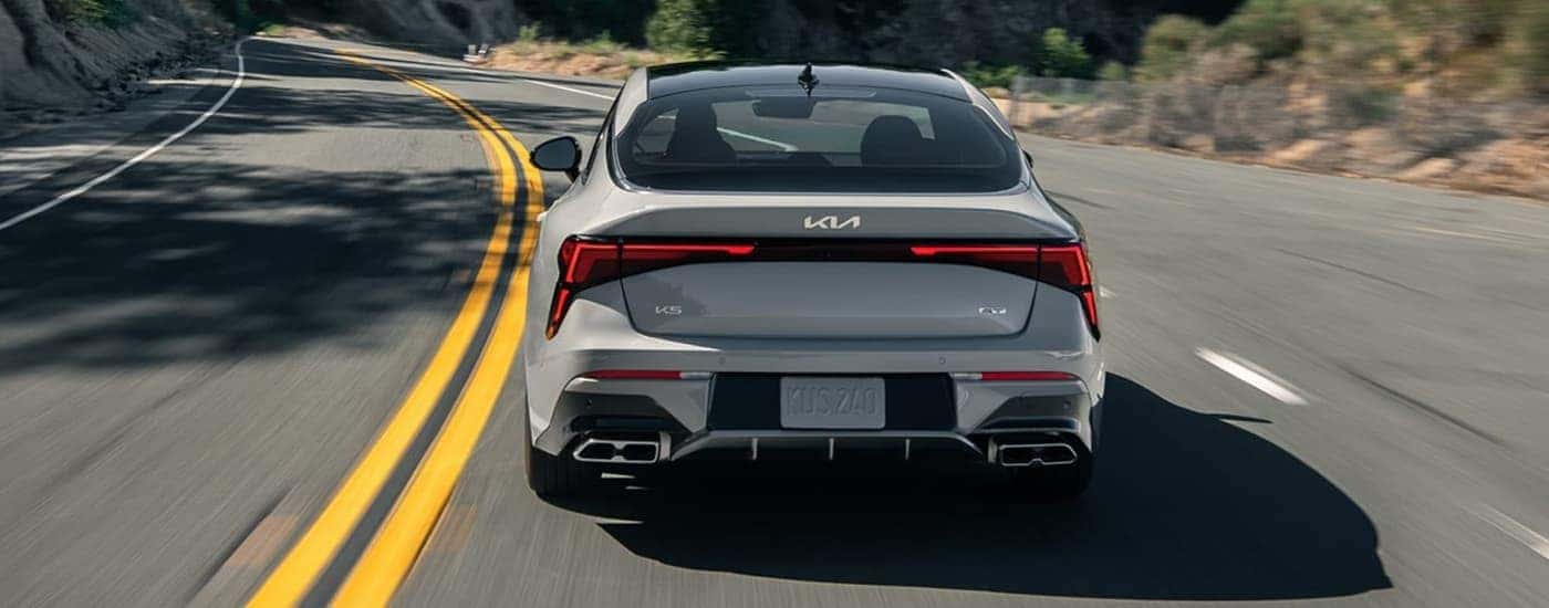 Rear of a grey 2025 Kia K5 GT driving on a winding road.