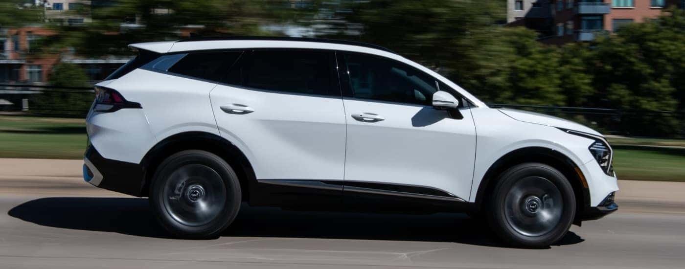A white 2023 Kia Sportage Hybrid driving on a city street.