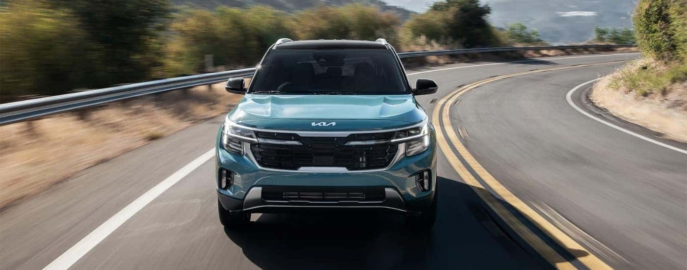 A blue 2025 Kia Seltos for sale is shown driving on a highway.