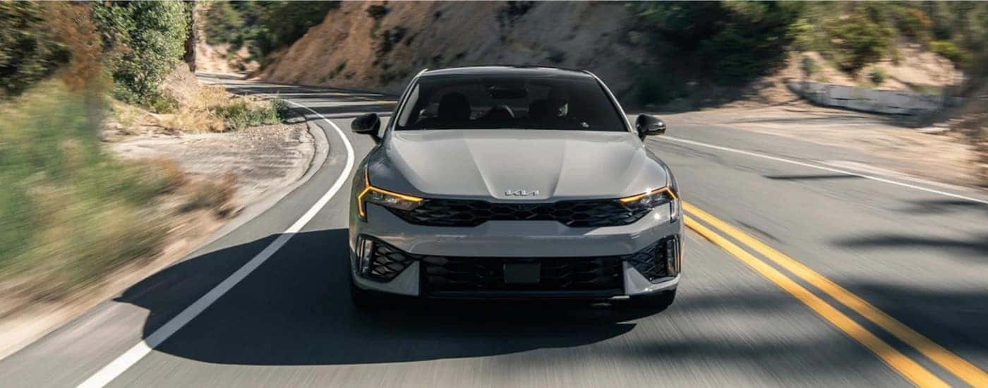 A gray 2024 Kia K5 is shown driving to a Kia dealer near Alcoa.