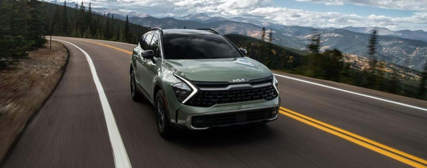 A green 2023 Kia Sportage is driving on a mountain road.