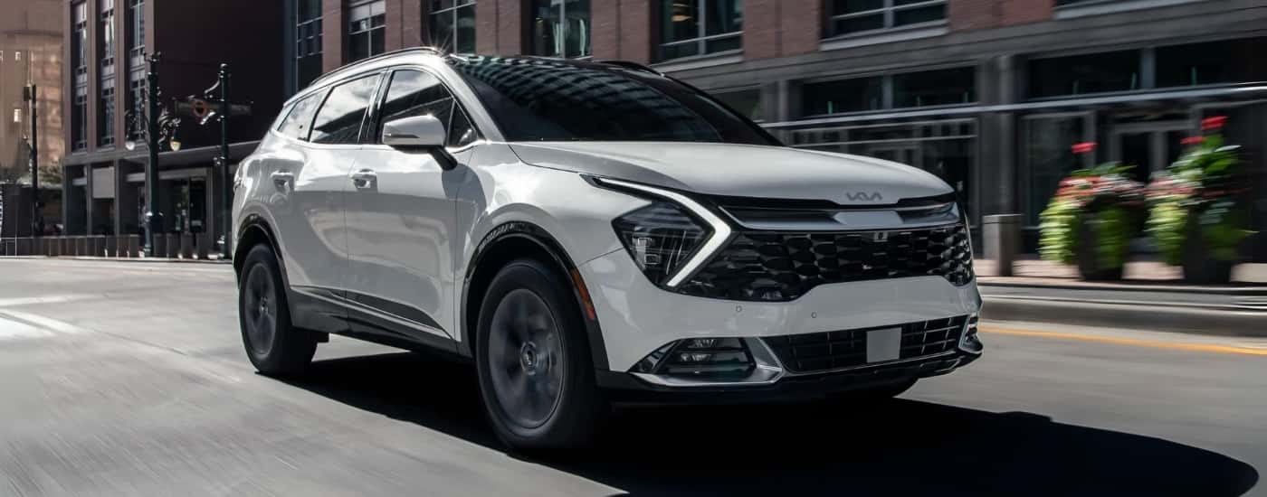 A white 2024 Kia Sportage Hybrid driving in a city.