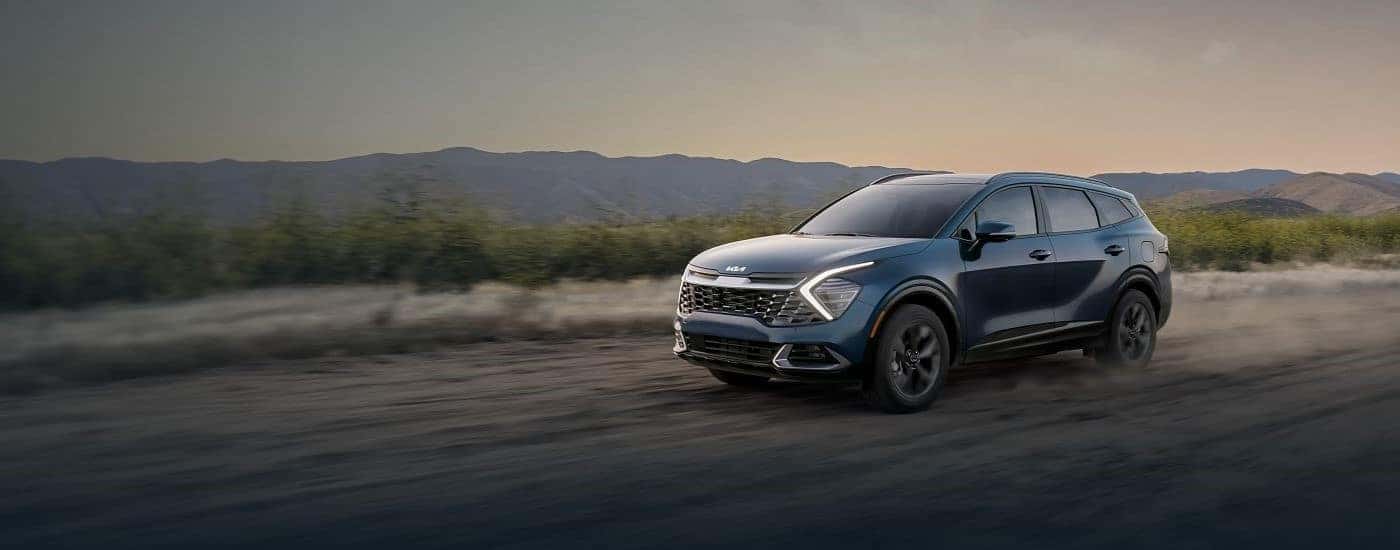 A blue 2024 Kia Sportage driving off-road on dirt
