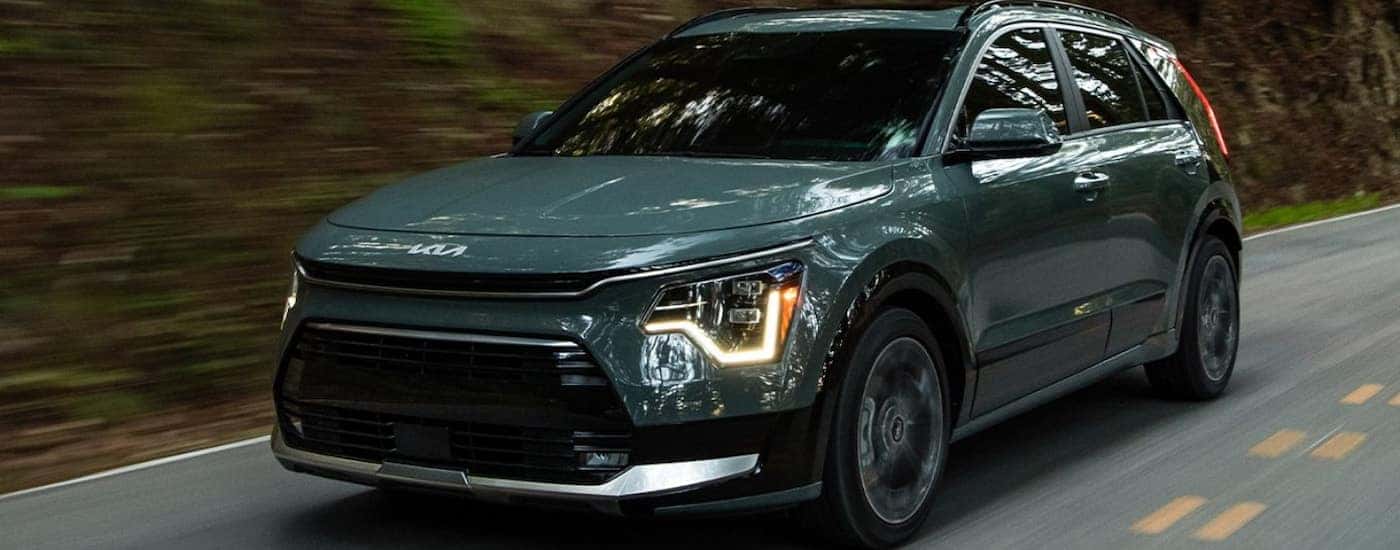 Green 2025 Kia Niro driving down a road through a forest.
