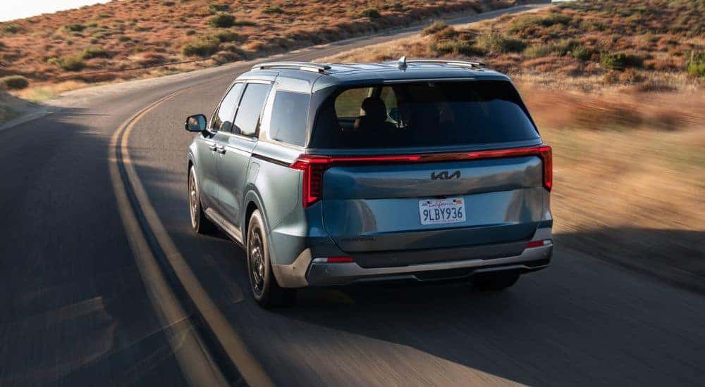 Blue 2026 Kia Carnival rear view as it drives down the road