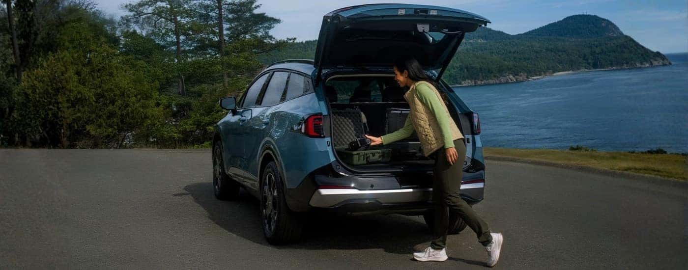 Person with a camera near a blue 2026 Kia Sportage HEV