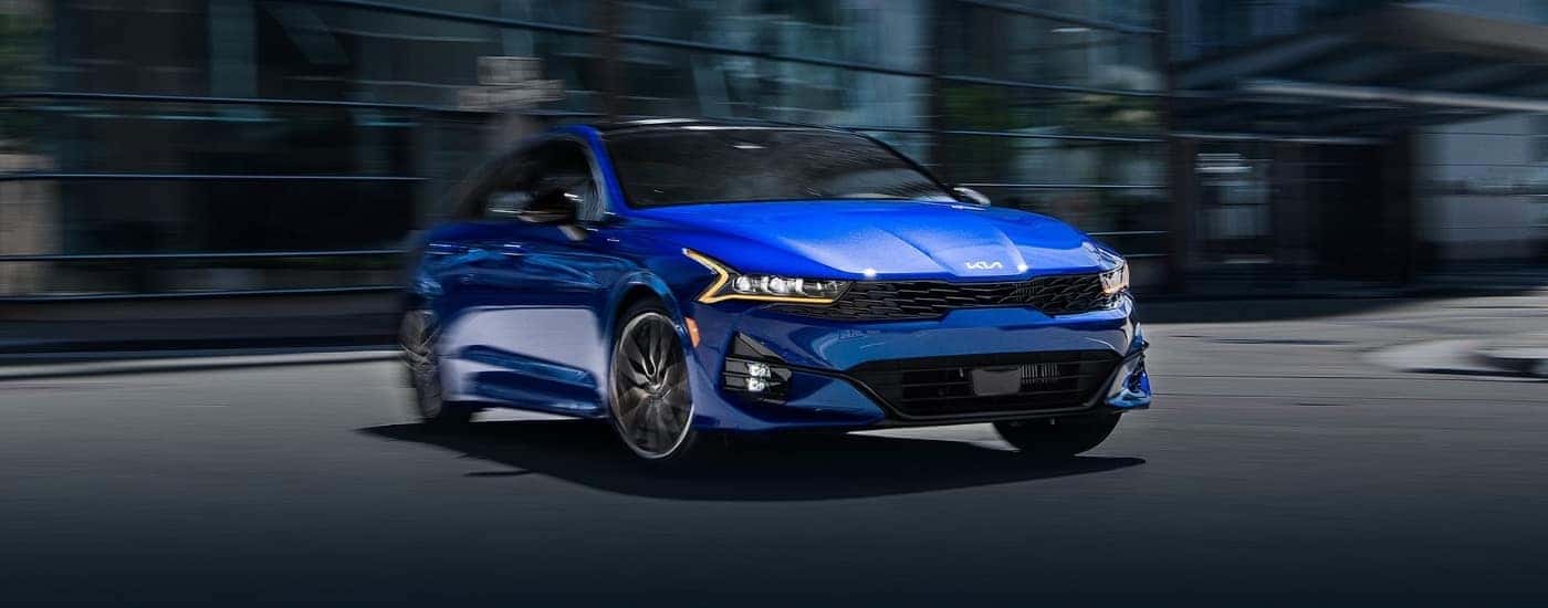 A blue 2025 Kia K5 driving in a city