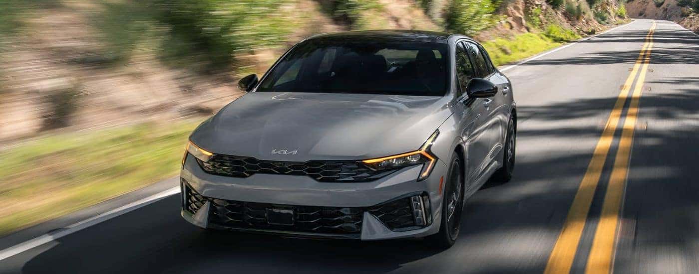 Grey 2026 Kia K5 driving on a paved road.