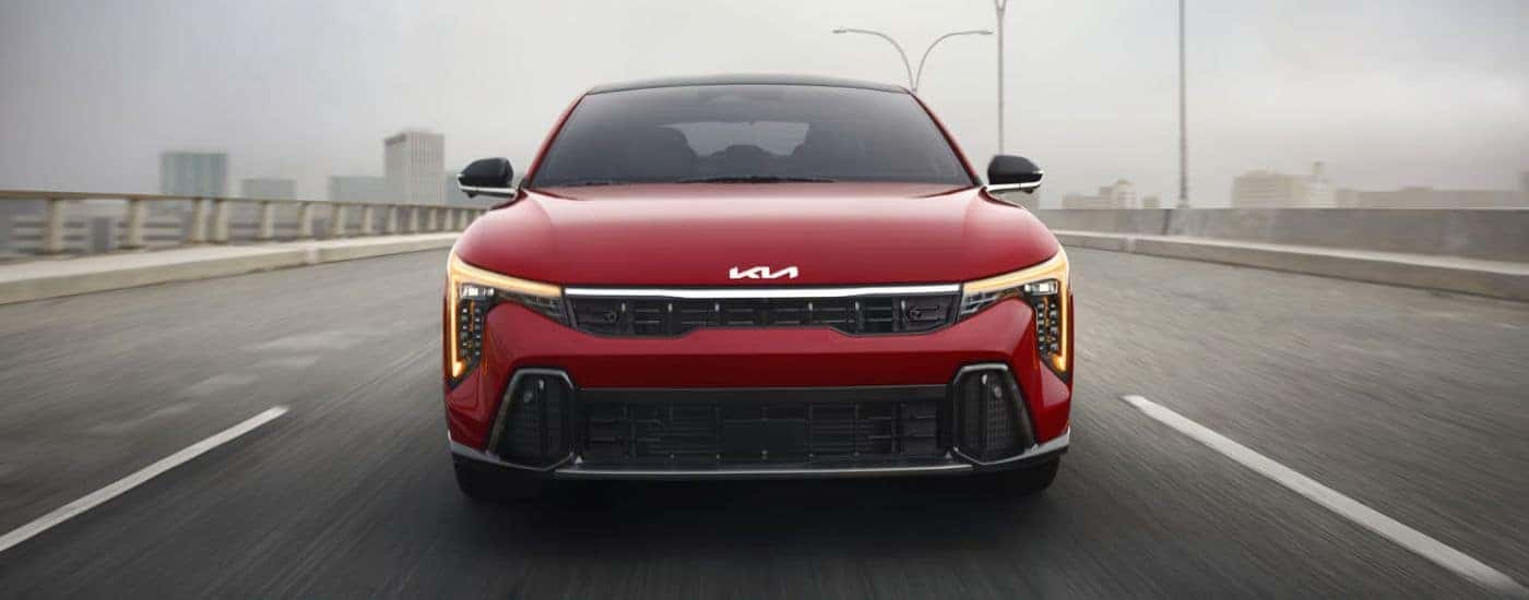 A red 2026 Kia K4 GT-Line Turbo shown driving head-on over a bridge.