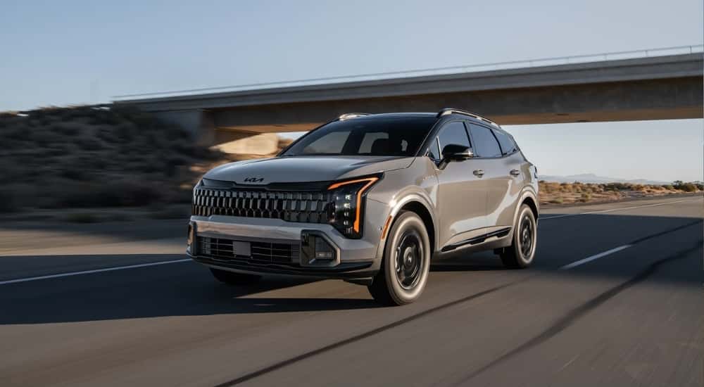 A gray 2026 Kia Sportage X-Pro Prestige driving under a bridge.