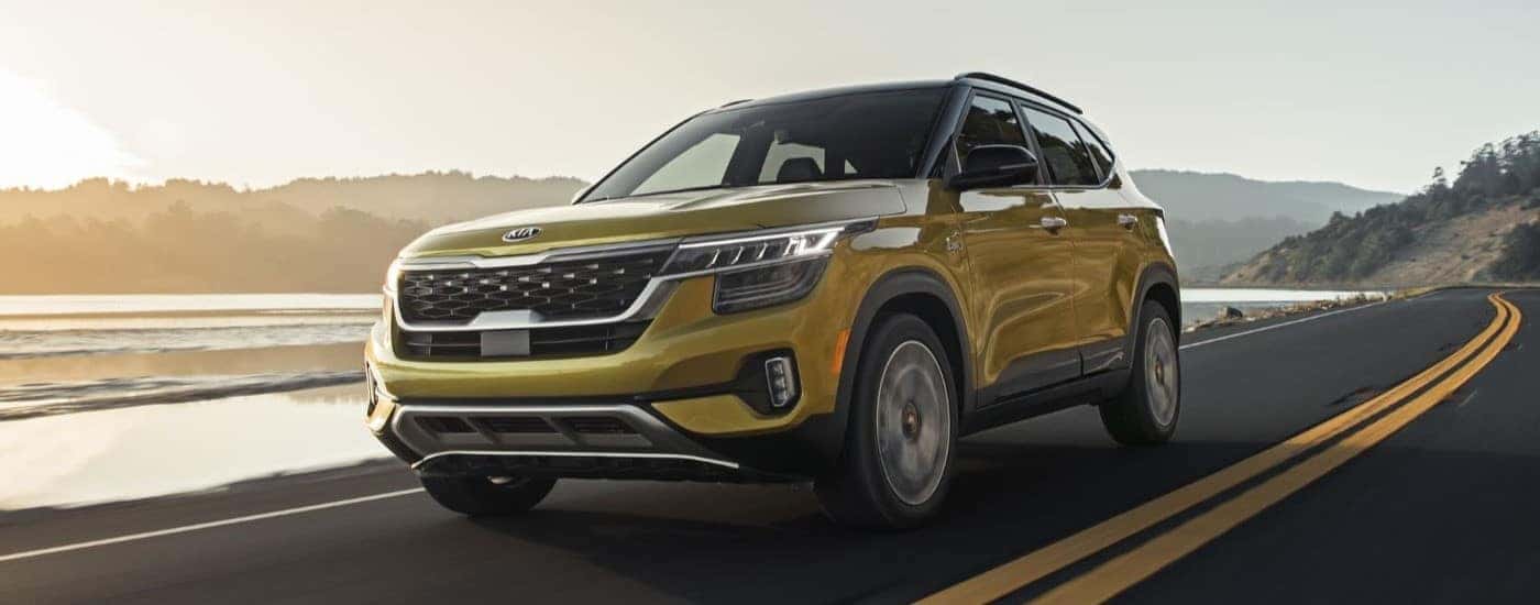 A yellow 2021 Kia Seltos driving by a lake.