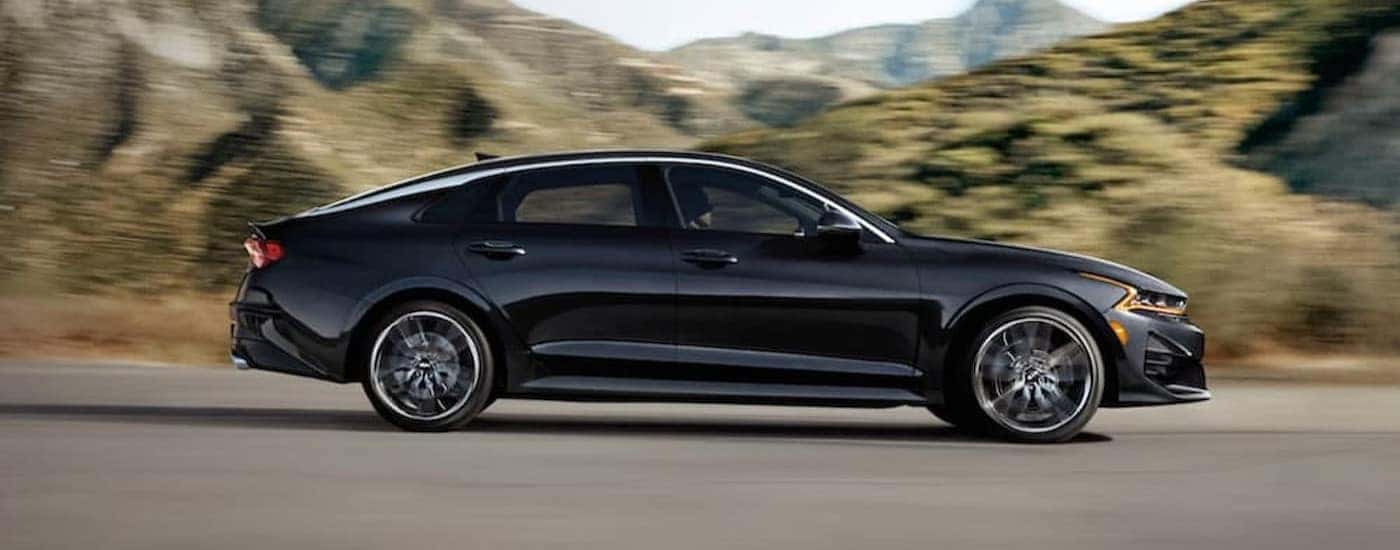 A black 2021 Kia K5 driving on a highway.
