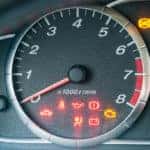 Closeup of car dashboard with many illuminated warning indicators.