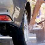 Perspective side view of man's hand using high pressure water jet to washing his car outside of home at morning time, self car washing concept