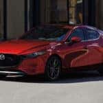 Red 2020 Mazda3 Hatchback parked with woman wearing white shirt out of focus in front of it
