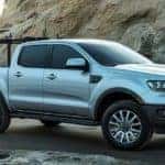 Surfer loading surf board into bed of 2019 Ford Ranger by rocky shore