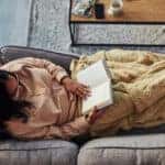 High angle shot of a young woman reading a book on the sofa at home