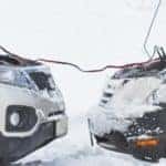 two cars in the snow, their batteries connected with jumper cables
