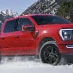a red F-150 tows snowmobiles on a trailer through snow