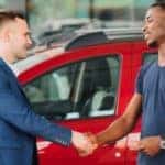 a couple shakes hands with a car salesman in a dealership