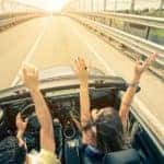 Happy couple driving on the road into the sunset in a sports car